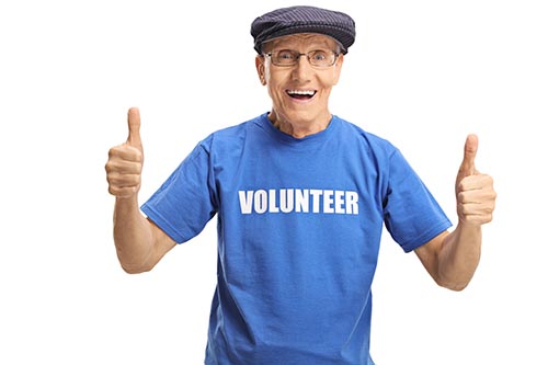 Cheerful elderly male volunteer in a blue t-shirt showing thumbs